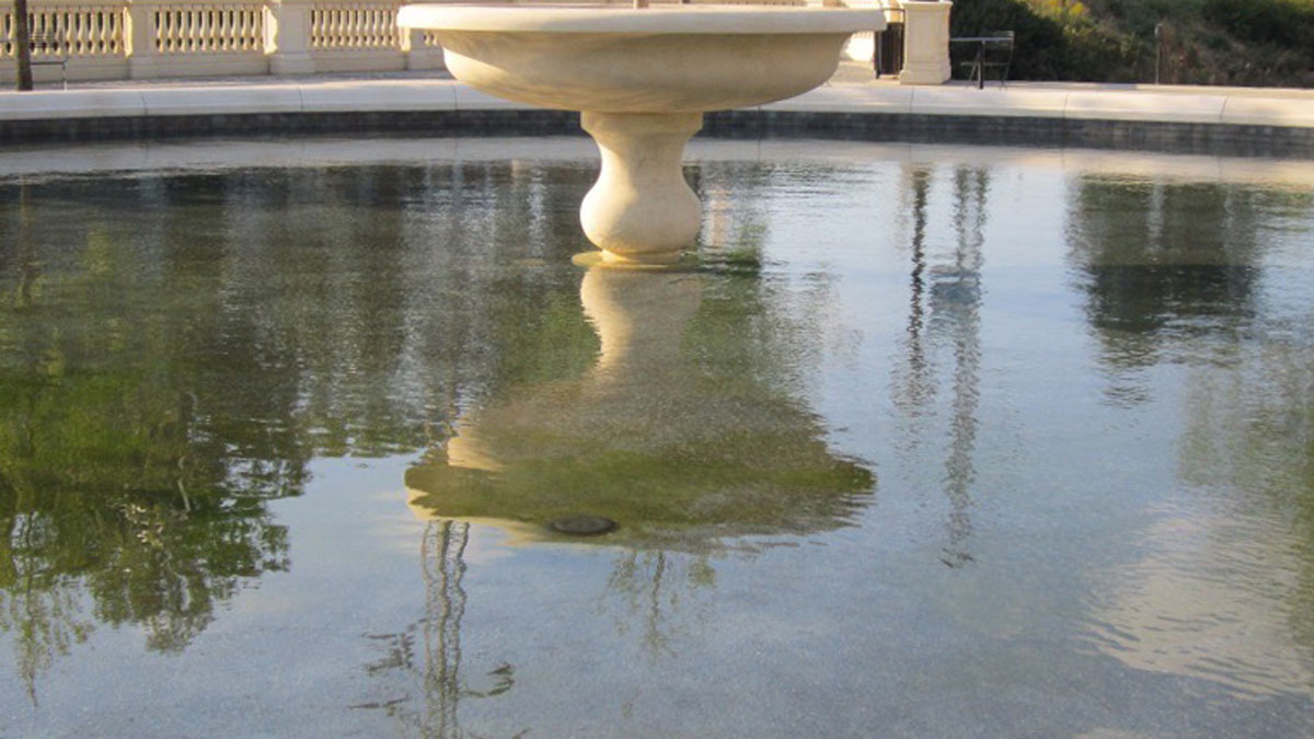 Watery reflection of a round concrete fountain base in a still fountain.